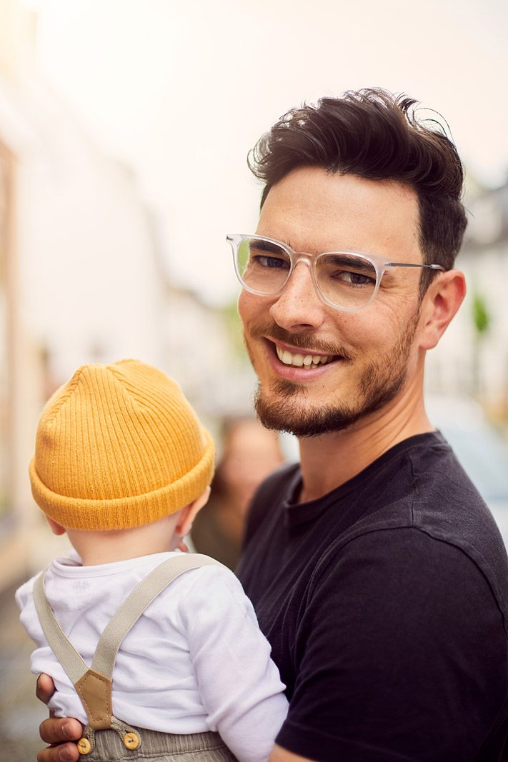 Vater mit Kind auf dem Arm blickt lächelnd in die Kamera